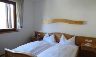 A bright bedroom with a wooden double bed. The room has a window with curtains and a bedside table next to the bed.