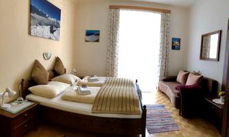 A cozy bedroom with a double bed, two pillows, and a bedspread. The room has large windows that let in plenty of daylight, and an inviting seating area.