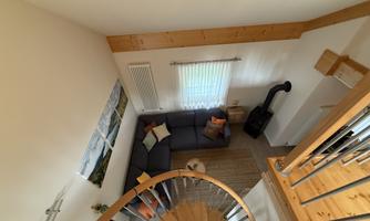 A cozy living room with a gray couch and decorative pillows. The room's height is accentuated by a spiral staircase and wooden details.