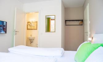 A bright room with a double bed and green cushions. In the background, a bathroom and a wardrobe can be seen.