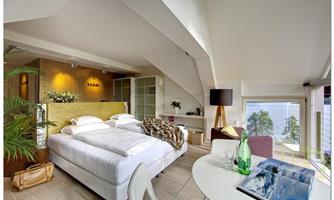 A modern bedroom with a large bed and a cozy living area. Large windows offer a beautiful view of nature.
