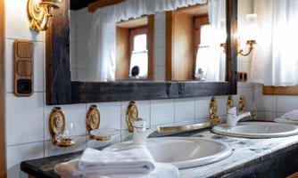 A modern bathroom with two sinks and a large mirror. There are gold fixtures and towels on the countertop.