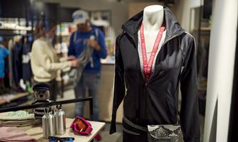A sporty outfit on a mannequin with a black jacket and a medal. In the background, other customers are seen in the store.
