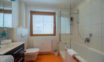 A modern bathroom with a shower and a bathtub. Bright tiles and a window provide plenty of light.