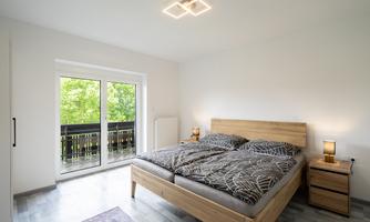 A modern bedroom with a double bed and wooden details. Large windows bring in plenty of daylight and offer a view of the greenery.