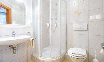 A modern bathroom with a shower cabin and a sink. The walls are tiled with light tiles and the space feels clean and friendly.