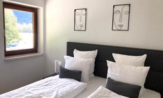 A modern bedroom with a double bed and two framed faces on the wall. The bedding is white with gray cushions.