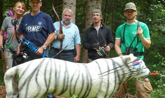 A group of five people stands in the forest holding bows with arrows. In front of them is a replica white tiger that has been shot with arrows.