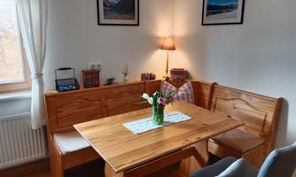 A cozy dining area with a wooden farmhouse table and benches. On the table is a vase with fresh flowers, and in the background, pictures are hanging on the wall.