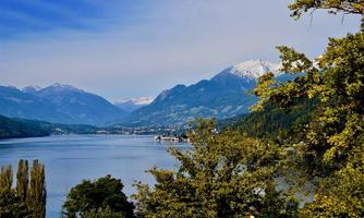 A picturesque lake surrounded by mountains and trees. The sky is clear and the snow-capped peaks of the mountains are visible.
