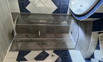 A modern bathroom with a glass shower cabin and a whirlpool bathtub. The walls are decorated with blue and white tiles.