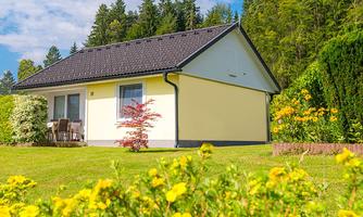 A beautiful house surrounded by colorful flowers and green grass. In the background, there are trees and a clear blue sky.
