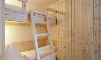 A cozy bedroom with a bunk bed made of light wood. The room features a large wardrobe and has a friendly atmosphere.