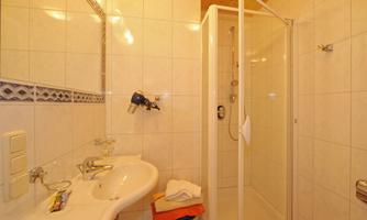 A modern bathroom with a shower area and a sink. The walls are tiled, and there is a wooden ceiling.