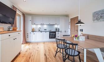 A modern kitchen with white cabinets and wooden flooring. A dining table with black chairs invites you to linger.