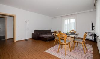 A modern living room with a cozy couch and a dining table. Large windows provide plenty of natural light.