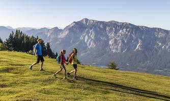 Three hikers are enjoying a sunny day in the mountains. In the background, majestic mountains and a clear sky can be seen.