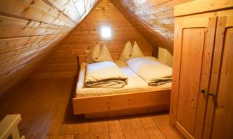 A cozy attic bedroom with wooden paneling. The room contains a double bed with two pillows and a wardrobe.