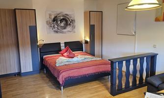 A bright and modern bedroom with a large bed and wooden floor. The furnishings include a television and a cozy seating area.