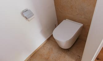A modern bathroom with a simple toilet and a minimalist design. The floor is made of light-colored material, and the walls are white.