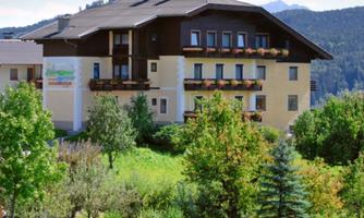 A cozy building surrounded by green trees and meadows. In the background, mountains are visible, creating a beautiful landscape.