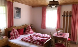 A cozy bedroom with a double bed and checkered pillows. There is a table with chairs and rustic decoration.