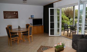 A friendly living and dining room with a table and chairs. Large windows open up to a beautiful outdoor area with patio furniture.