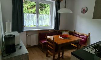 A cozy kitchen area with a table and chairs. Large windows let in plenty of light and offer a view of the greenery.