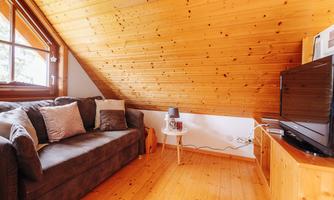 A cozy living room in the attic with a wooden ceiling. There is a sofa, a small table, and a television.