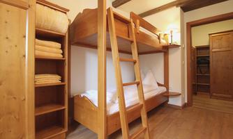 A cozy bedroom with a wooden bunk bed and a ladder. In the background, there are shelves with towels and an open cupboard.