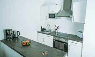A modern kitchen with white cabinets and a gray countertop. On the counter, there is a fruit bowl and a coffee machine.