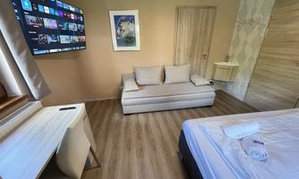 A modern room with a large television on the wall and a cozy sofa. The floor is made of wood and the room is bright and inviting.