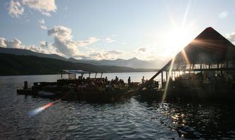 A beautiful lake with a wooden pier and a sun terrace. The sun sets behind the mountains and casts a warm light on the water.