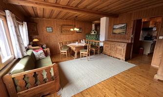 A cozy room with wooden paneling and a dining area. The decor is rustic with a carpet and windows that provide plenty of daylight.
