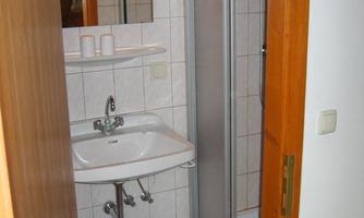A small bathroom with a shower, a sink, and a mirror. The walls are tiled and the floor has a blue carpet.