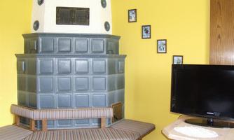 A cozy living space with a gray tiled stove and a television. The walls are painted in a cheerful yellow and there are some pictures hanging.