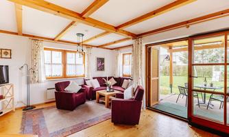 A cozy living room with red armchairs and a wooden table. Large windows provide a view of the garden.