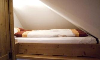 A cozy bed in the attic with a slanted roof and warm colors. The bedding is light and the atmosphere is inviting.