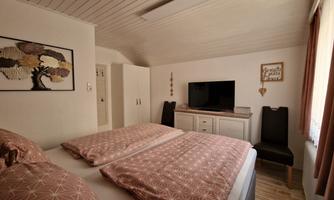 A cozy bedroom with two beds and a television. The walls are kept light and there is a decorative picture as well as windows with curtains.