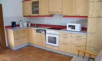 A bright kitchen with wooden cabinets and red accents. It is equipped with modern appliances like a stove, a microwave, and a refrigerator.