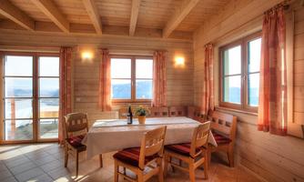 An inviting dining area in a wooden cabin, furnished with a table and chairs. Large windows offer a view of the landscape and let in plenty of light.