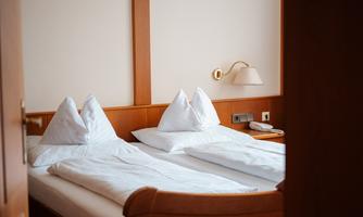 A cozy bedroom with two beds and traditional pillows. The wooden furniture and warm lighting create an inviting atmosphere.