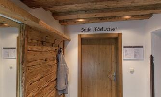 An inviting hallway with wooden paneling and a door sign indicating the "Edelweiss Suite." Some hooks and a towel are hanging on the wall.