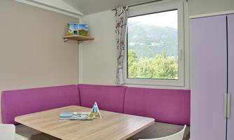 A cozy dining area with a purple bench and wooden table. Through the window, you can see the beautiful mountain landscape.