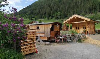 A rustic wooden house and a caravan surrounded by colorful flowers and green hills. The place conveys a cozy and inviting atmosphere.