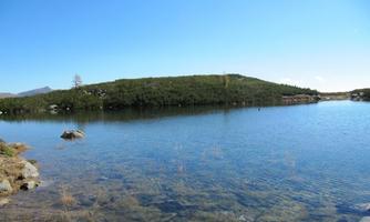 A tranquil lake surrounded by green hills and a clear sky. The water surface reflects nature.