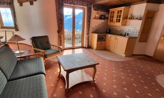 A cozy living room with a sofa, a coffee table, and an open kitchen. Large windows let in plenty of light and offer a view of the mountains.