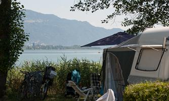 A beautiful campsite by the lake with a view of the mountains. Bicycles and camping furniture are visible in the foreground.