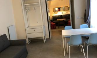 A modern apartment with a cozy sofa and a dining area. There is a bright kitchen in the background.