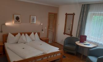 A cozy bedroom with a double bed and several pillows. There is a small table with two chairs and a large window with curtains.